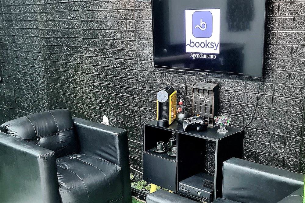 Lounge de espera com poltronas de couro, TV com agendamento Booksy e videogame